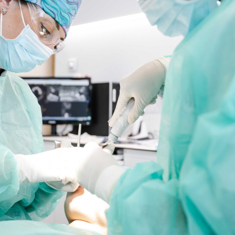 From above crop professional dentists in latex gloves using clean tools to perform oral procedure on unrecognizable patient in contemporary clinic